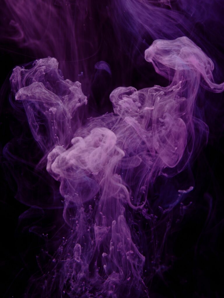 Vibrant purple ink swirling in water against a dark background, creating an abstract and artistic effect.