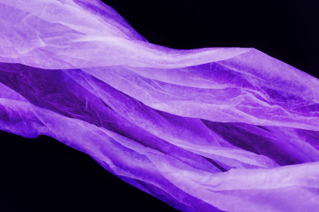 Abstract image of delicate purple chiffon waves against a black backdrop, creating a textured artistic effect.